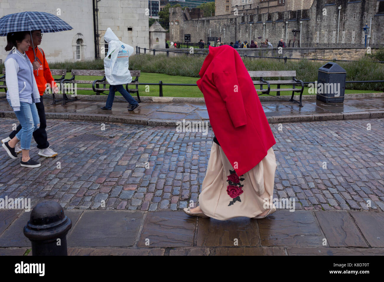 Eine touristische Dame deckt ihren Kopf mit einem roten Mantel, während andere tragen Regen-capes vor dem Tower von London entfernt, am 14. September 2017 in London, England. Über viele Jahrhunderte, der Turm sah unzählige Hinrichtungen und Enthauptungen von Angeklagten und von Verrat und Verbrechen gegen den Staat versucht. Stockfoto