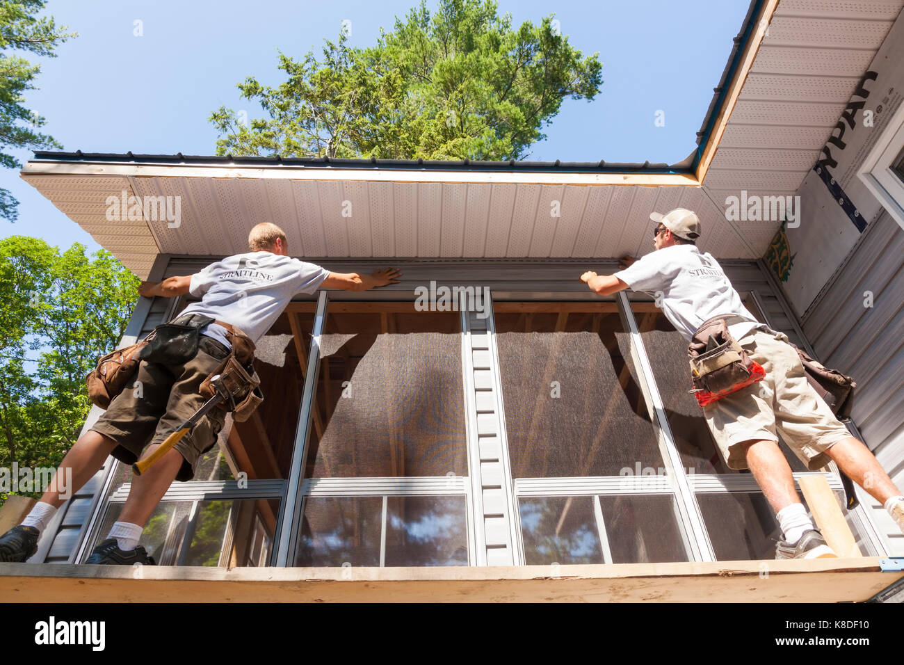 Zwei Bauarbeiter Installation ein Stück Vinyl Siding auf ein temporäres Gerüst in Ontario, Kanada. Stockfoto