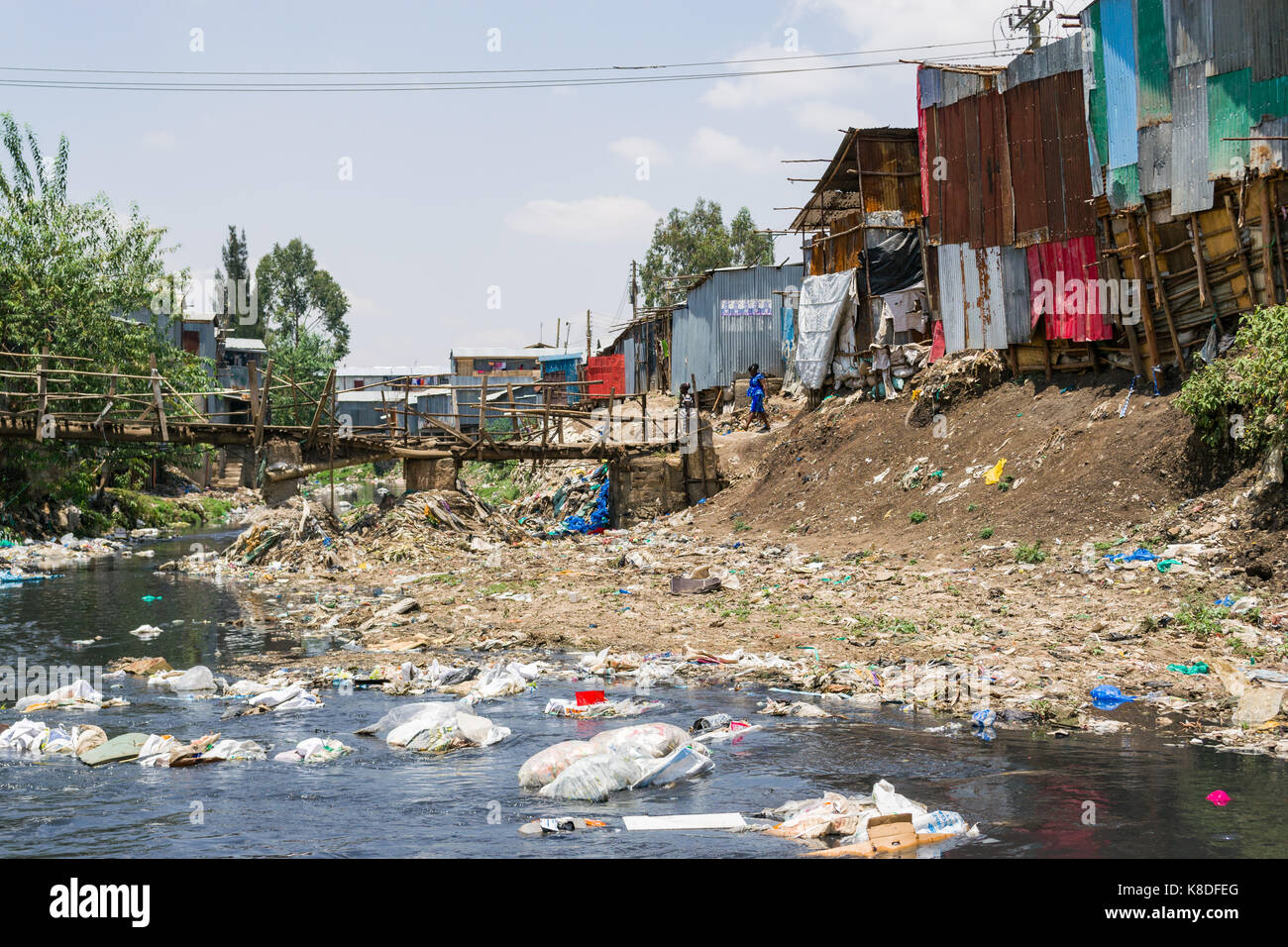 Slum Hütten Linie Ngong Fluss, der mit Müll verunreinigt ist, Kunststoff Abfall und Müll, eine provisorische Holzbrücke überquert es, Nairobi, Kenia Stockfoto