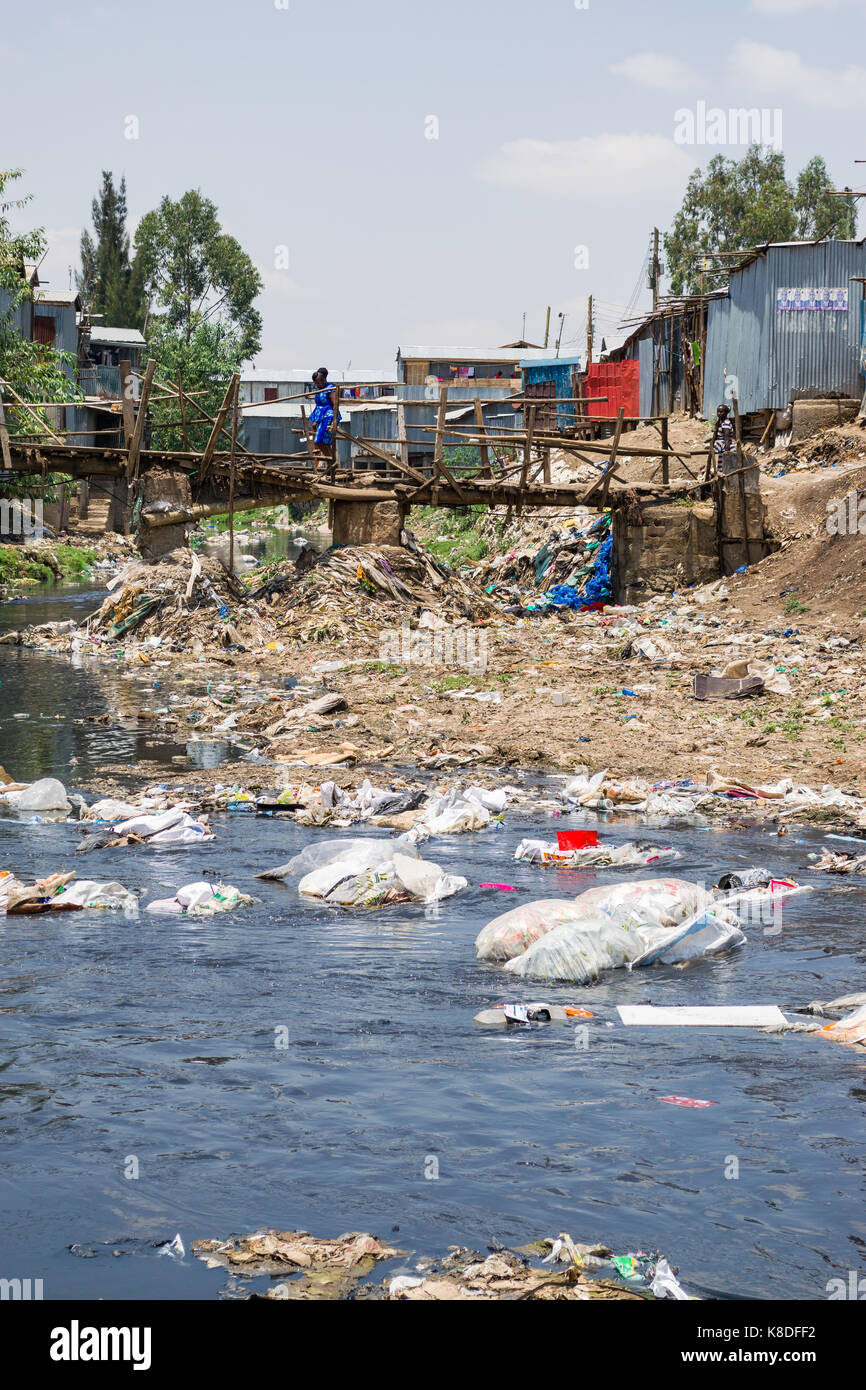 Slum Hütten Linie Ngong Fluss, der mit Müll verunreinigt ist, Kunststoff Abfall und Müll, eine provisorische Holzbrücke überquert es, Nairobi, Kenia Stockfoto