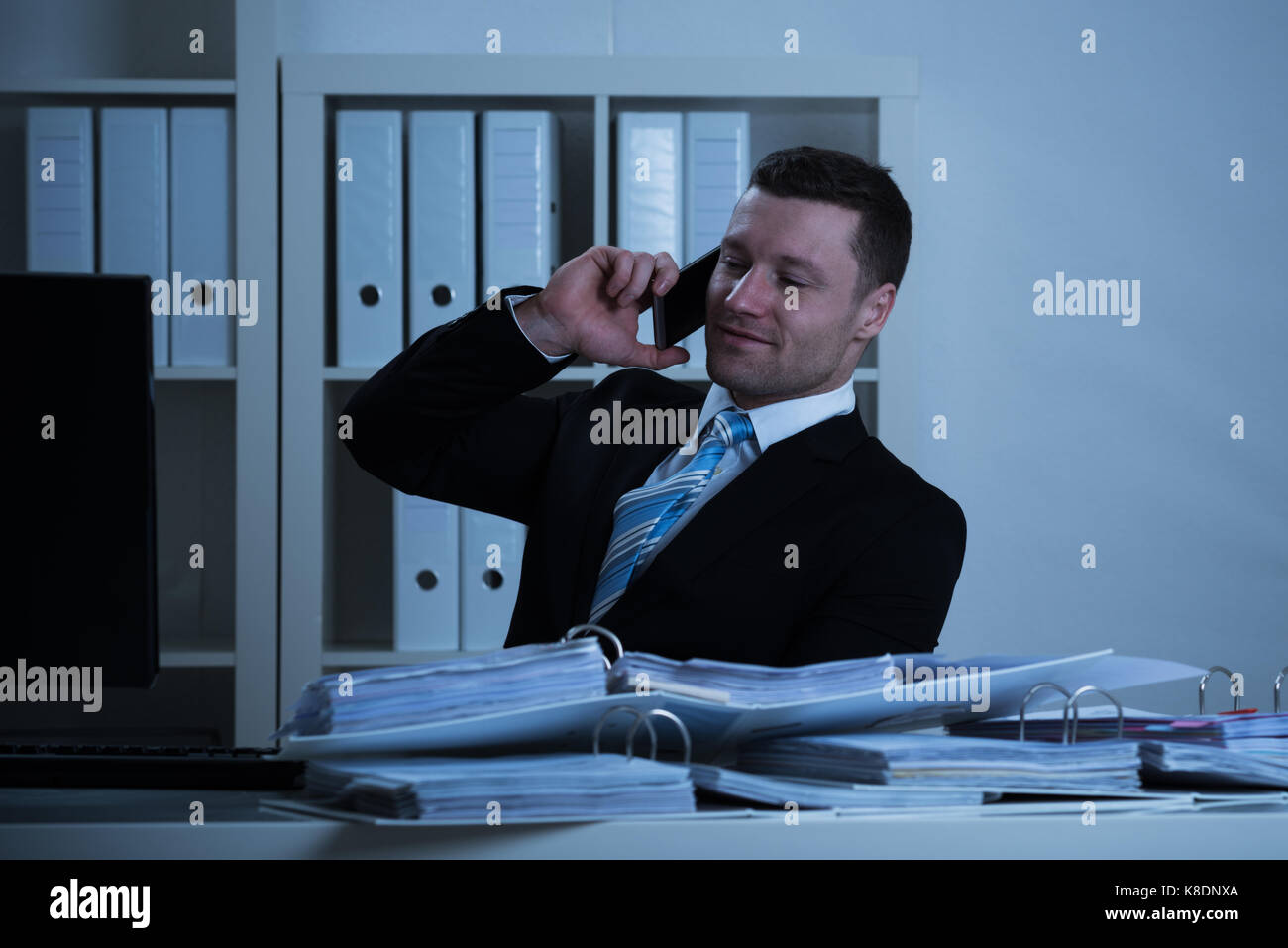 Lächelnd Geschäftsmann mit Smartphone, während spät am Schreibtisch im Büro arbeiten Stockfoto