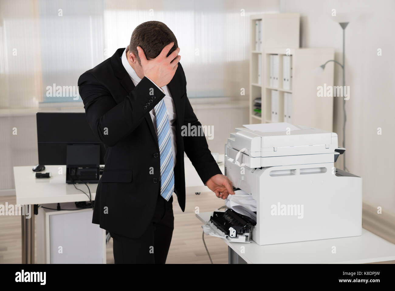 Gereizter Geschäftsmann auf Papier im Drucker im Büro fest suchen Stockfoto