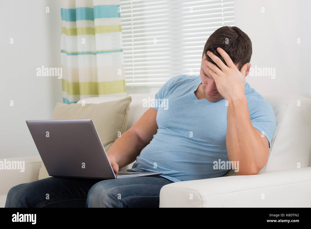 Verärgert Mitte der erwachsene Mann mit Laptop auf dem Sofa zu Hause Stockfoto