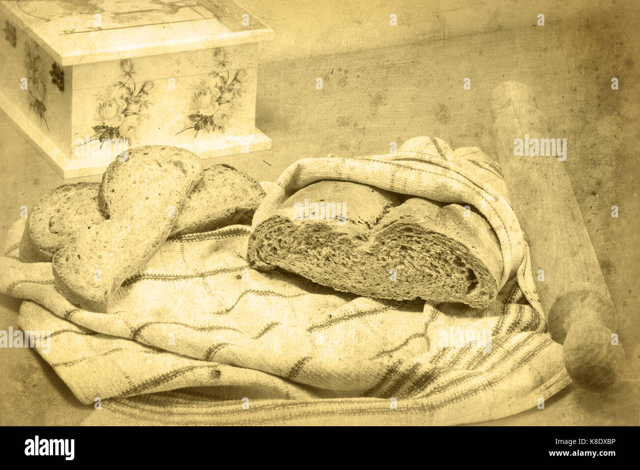 Brotlaib eingewickelt in ein Handtuch für die Küche, Rolling Pin, und zwei Scheiben Brot liegen auf dem Tuch. Decoupage Box ist teilweise sichtbar. Selektive konzentrieren. Stockfoto