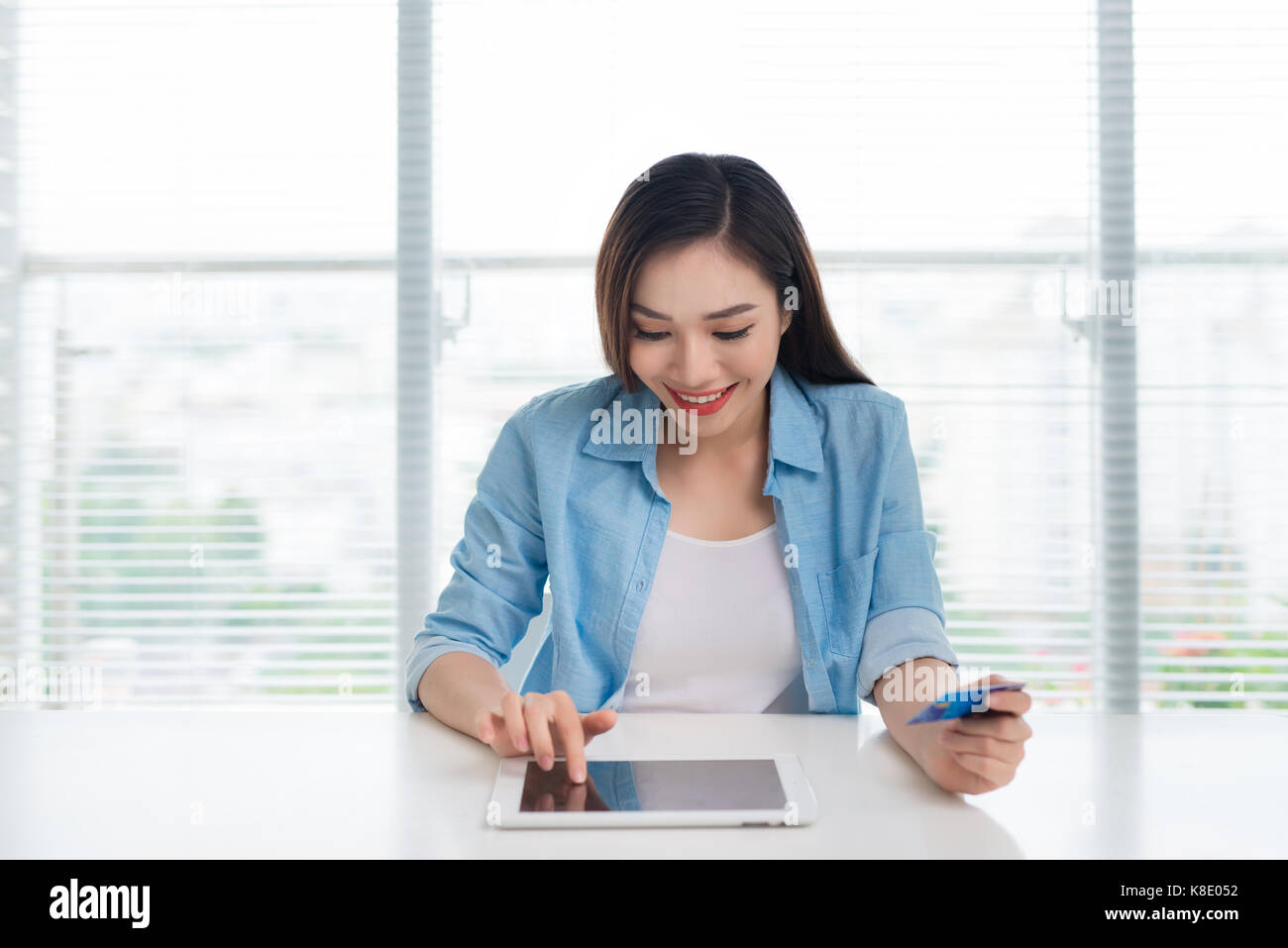 Frau sitzt in der modernen Home Office und mit Kreditkarte für die Zahlung über tablet device Stockfoto