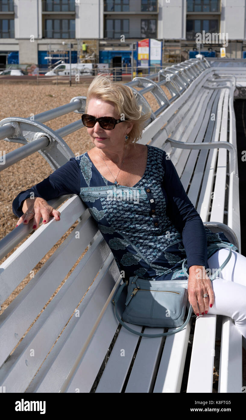 Frau alleine sitzen auf einem weißen Holz- sitz auf einem Meer Pier Stockfoto