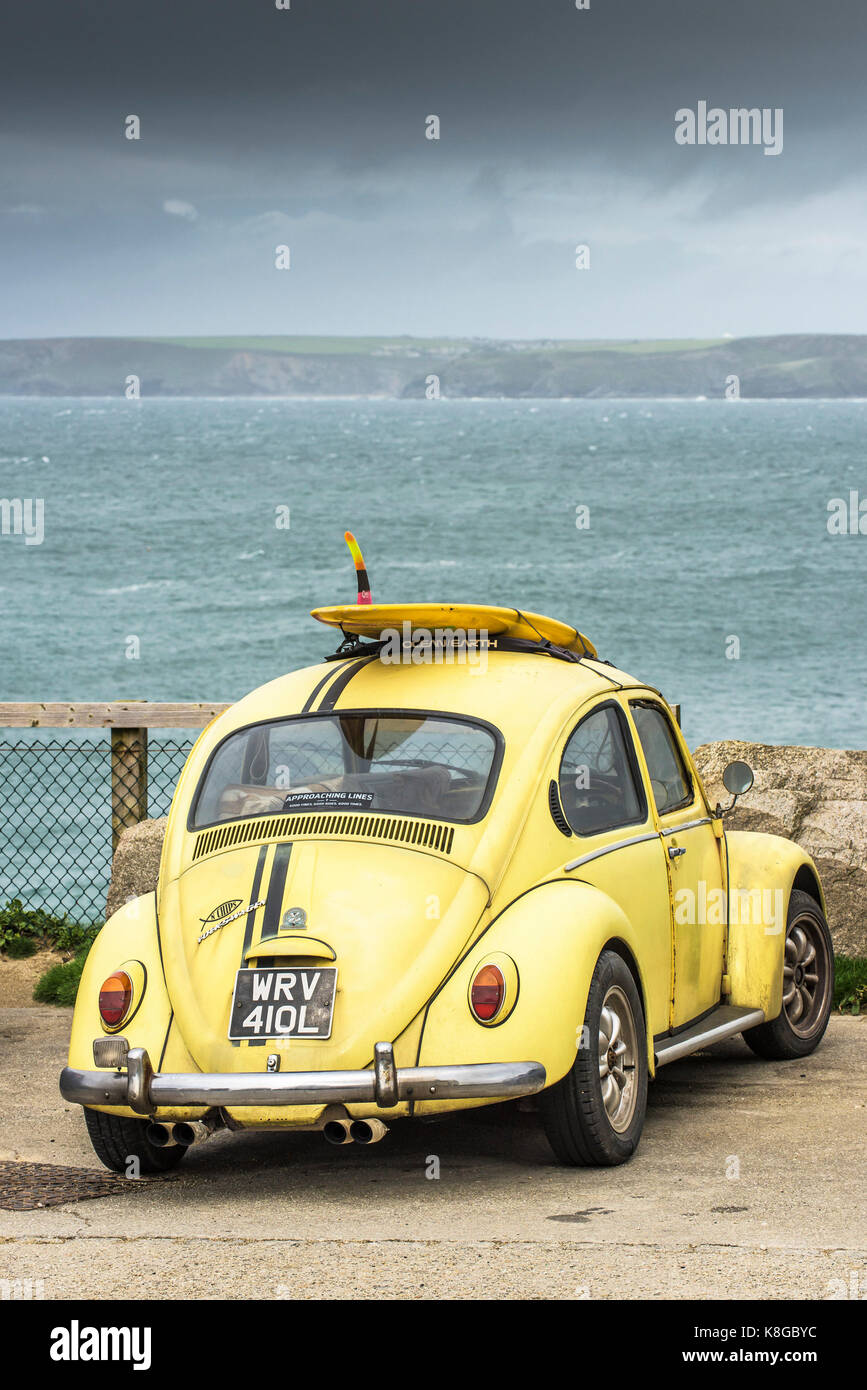 Volkswagen Auto - eine gelbe Volkswagen mit dem Surfbrett auf dem Dachgepäckträger in Little Fistral in Newquay, Cornwall geparkt Stockfoto