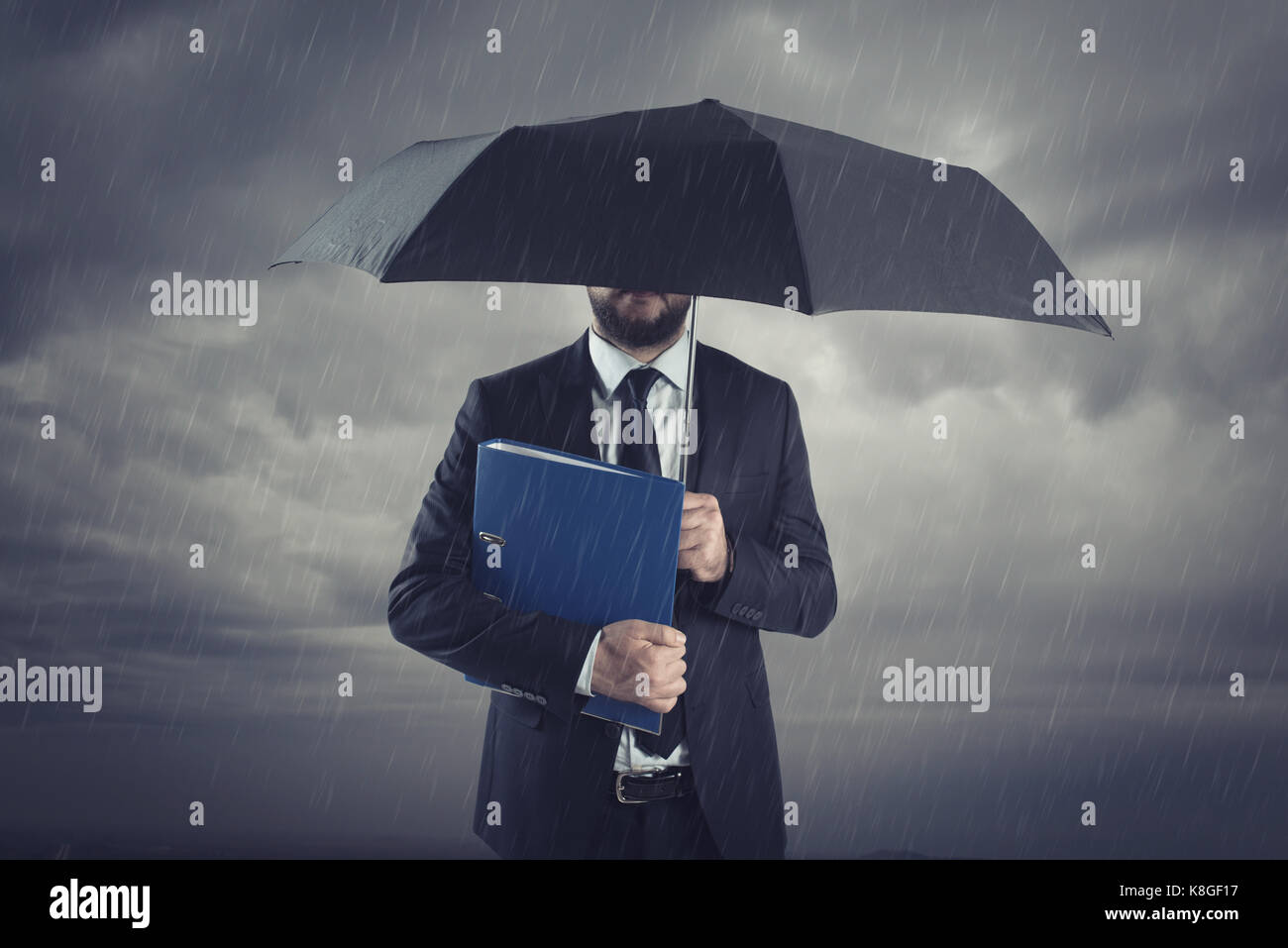 Unternehmer mit Regenschirm im stürmischen Regen. Versicherungsmakler und Berater in der Krisensituation. Stockfoto