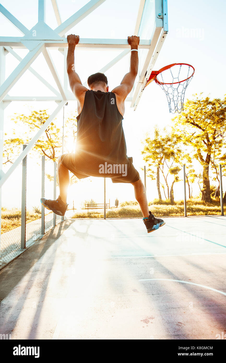 Junger Mann auf Basketball Court, Schwingen auf Basketball net Frame, Rückansicht Stockfoto