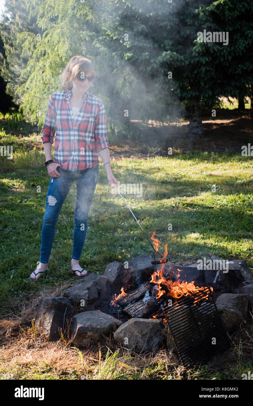 Frau stand neben Lagerfeuer, kochen Wurst in Flammen Stockfoto