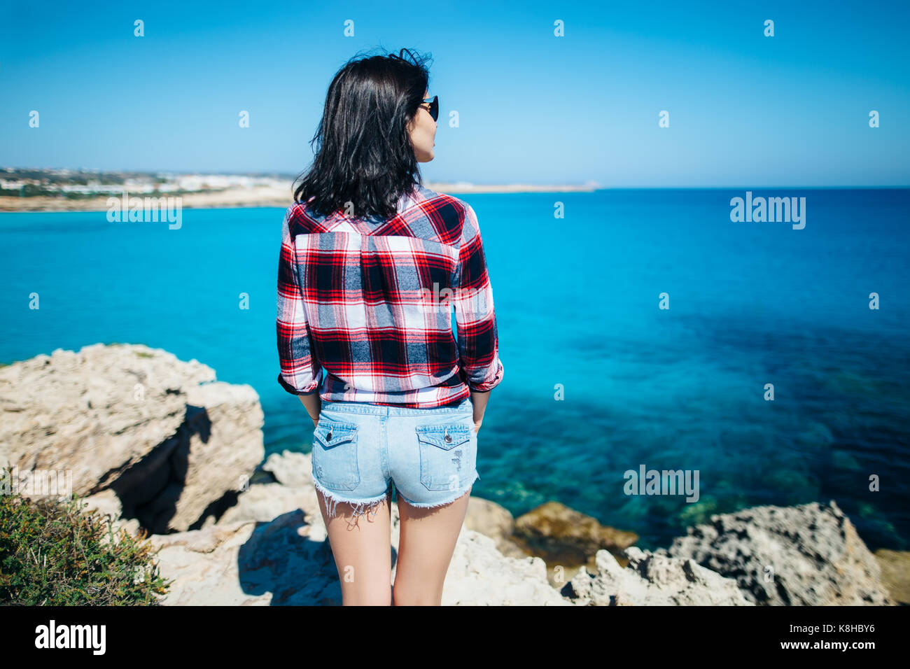 Rückansicht der jungen Frau mit dem Wind im Haar steht auf Felsen und genießen Sie einen wunderschönen Blick auf das Meer. Entspannen Konzept Stockfoto