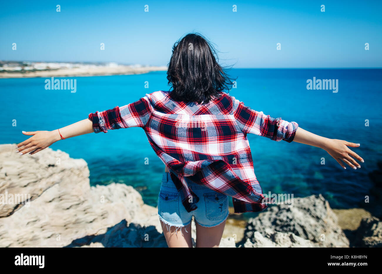Rückansicht der jungen Frau mit dem Wind im Haar ihre Hände heben auf der Klippe über dem Meer. Entspannen Konzept. Stockfoto