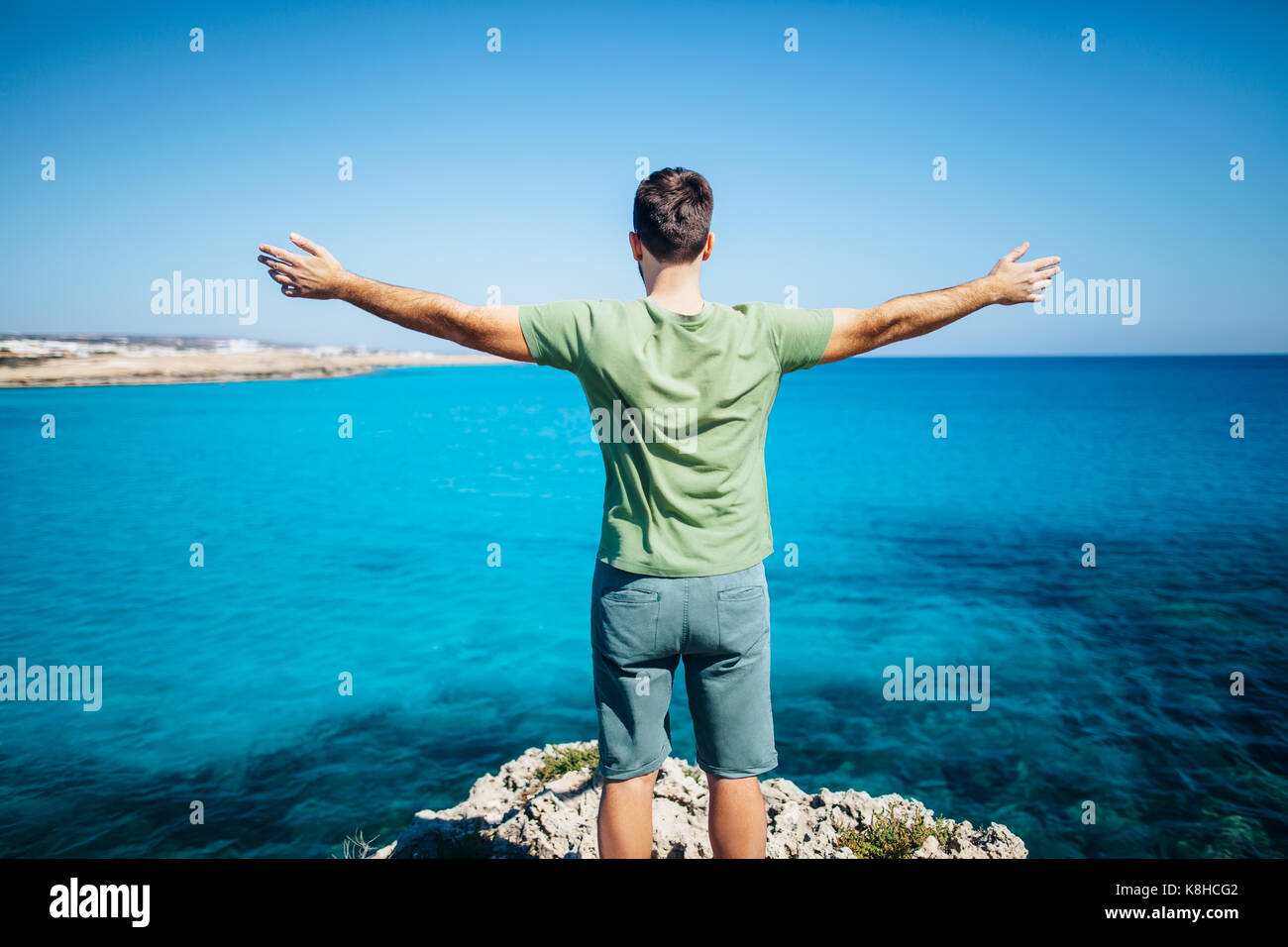 Rückansicht der junge Mann seine Hände auf der Klippe über dem Meer. Entspannen Konzept. Stockfoto