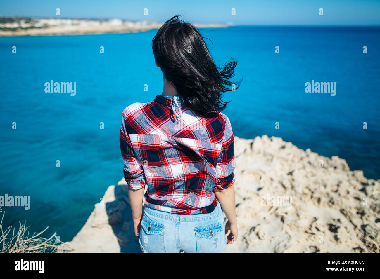 Rückansicht der jungen Frau mit dem Wind im Haar steht auf Felsen und genießen Sie einen wunderschönen Blick auf das Meer. Entspannen Konzept Stockfoto