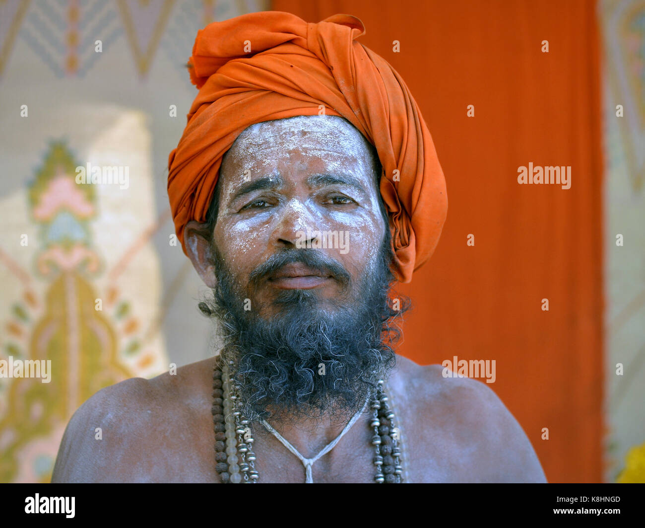 Junge indische Hinduistische sadhu mit orangefarbenen Turban und Heilige weiße Asche (vibhuti) alle über sein Gesicht und Bart Stockfoto