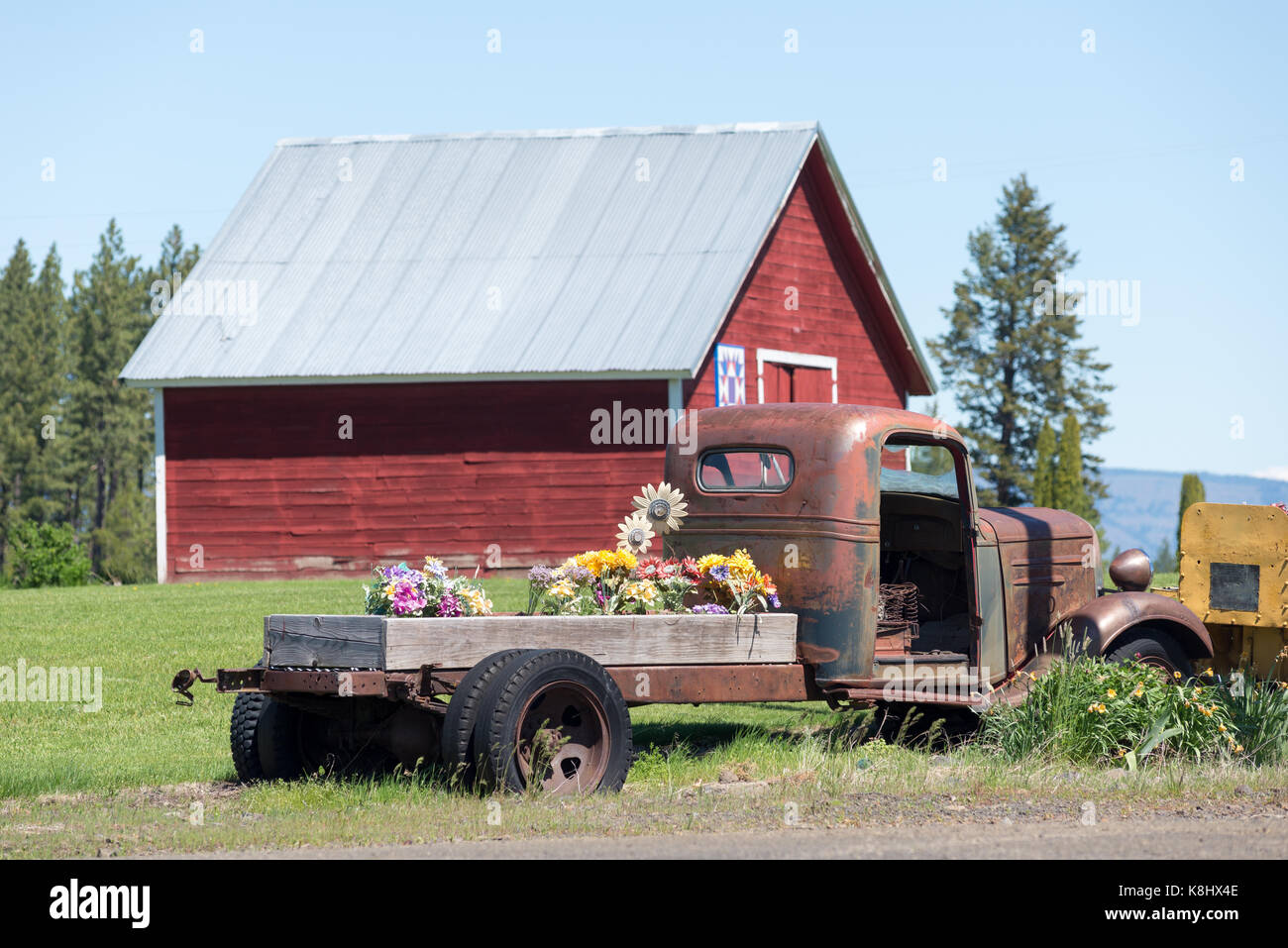 Alte Tieflader mit Plastikblumen vor einer Scheune in c Stockfoto