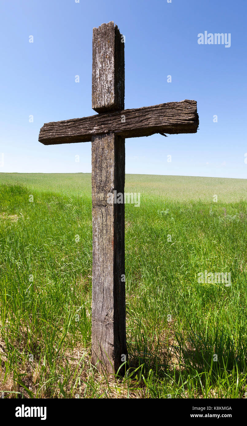 Alte, gesprungene Holzkreuz auf dem Feld. Sommer Zeit des Jahres. Blauer Himmel und grünes Gras im Hintergrund, auf dem christlichen Kreuz Fokus Stockfoto