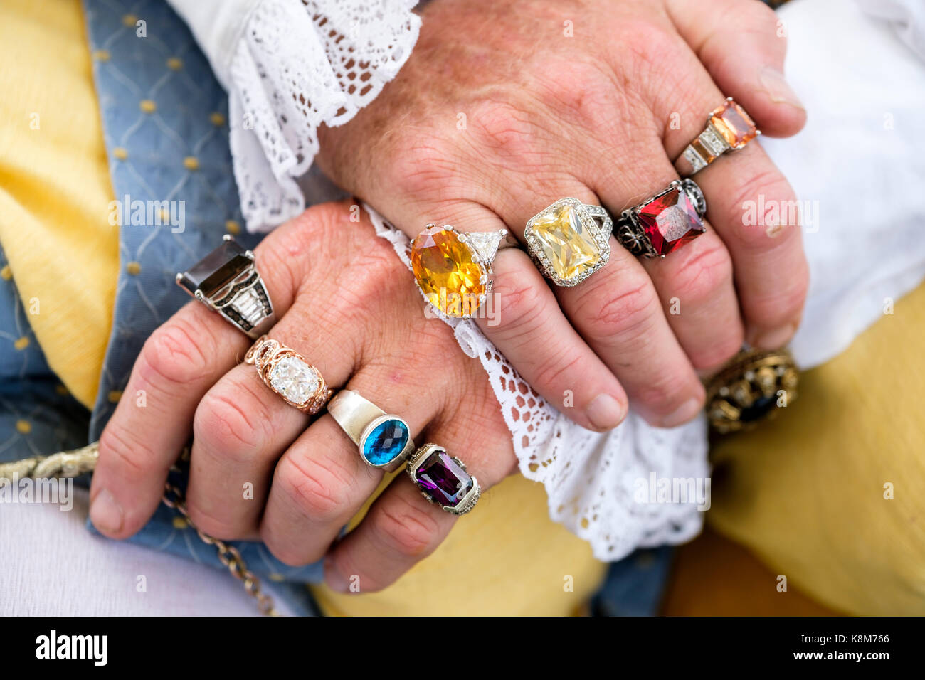 Männliche Hände mit den Fingern mit mehrfarbigen Halbedelstein Ringe in einem Renaissance Festival in Oxford, Ontario, Kanada geschmückt gekreuzt. Stockfoto