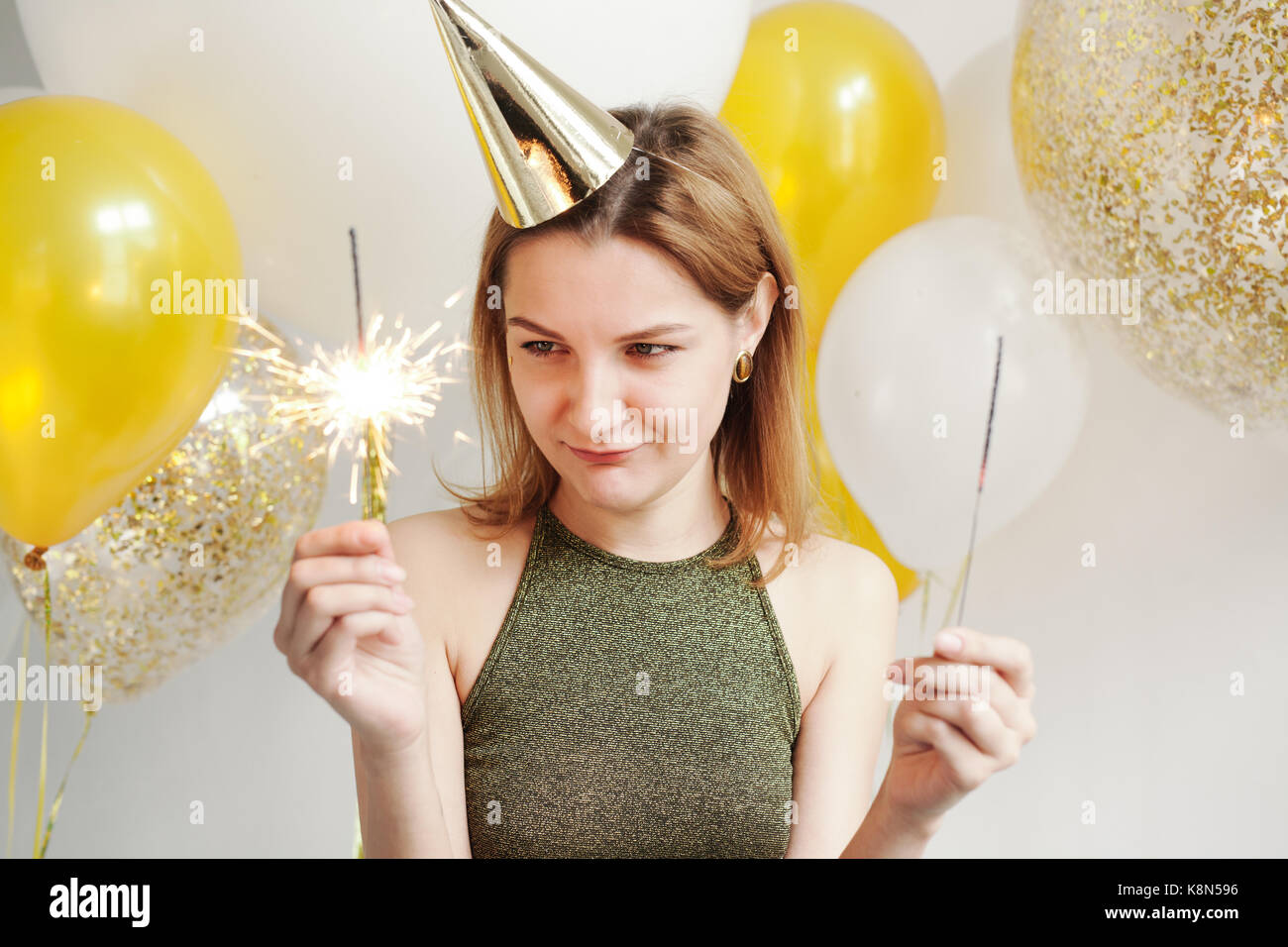 Junge Frau in einem feierlichen Kappe um Narren an einer Partei auf dem Hintergrund sinkender Konfetti Stockfoto