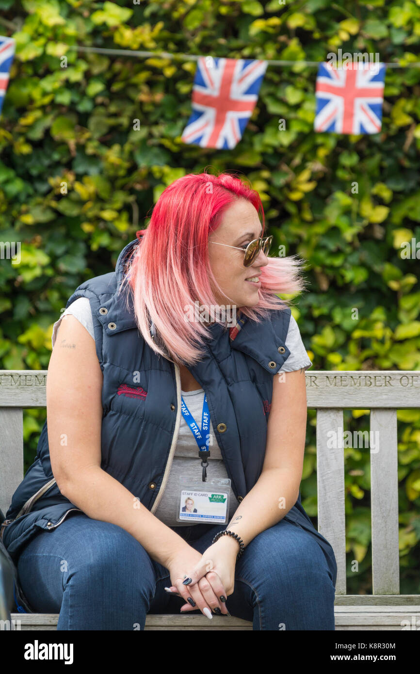 Junge Frau mit rot gefärbten Haaren auf einer Bank sitzen. Stockfoto