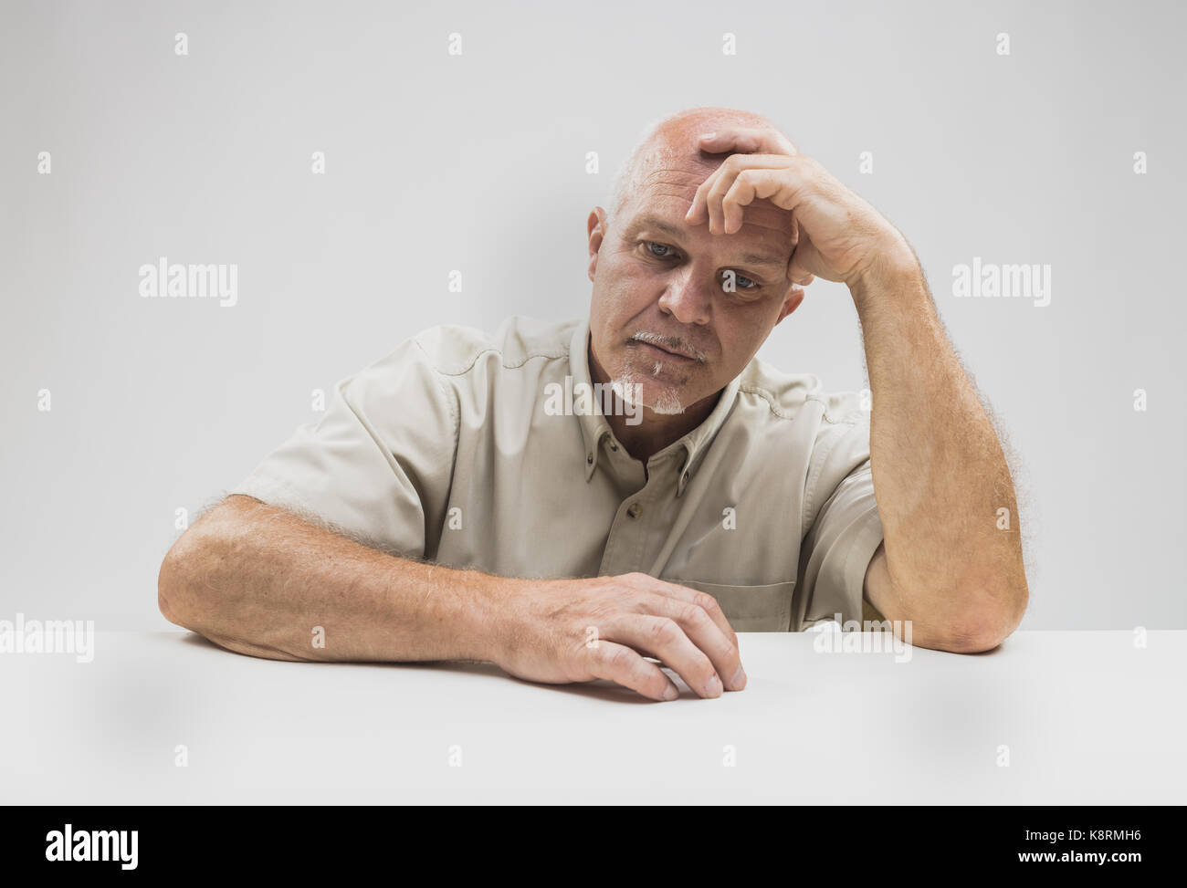 Mutlos älterer Mann denken mit seinen Kopf auf seine Hand, starrte auf den Tisch mit einem ernsten Ausdruck Stockfoto