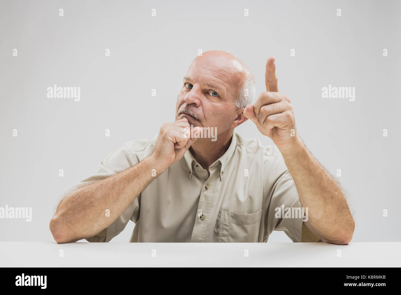 Emphatischen senior ein und deutete mit seinem Finger anspruchsvolle Aufmerksamkeit, wie er schaut, seitlich an der Kamera mit einem intensiven Ausdruck Stockfoto