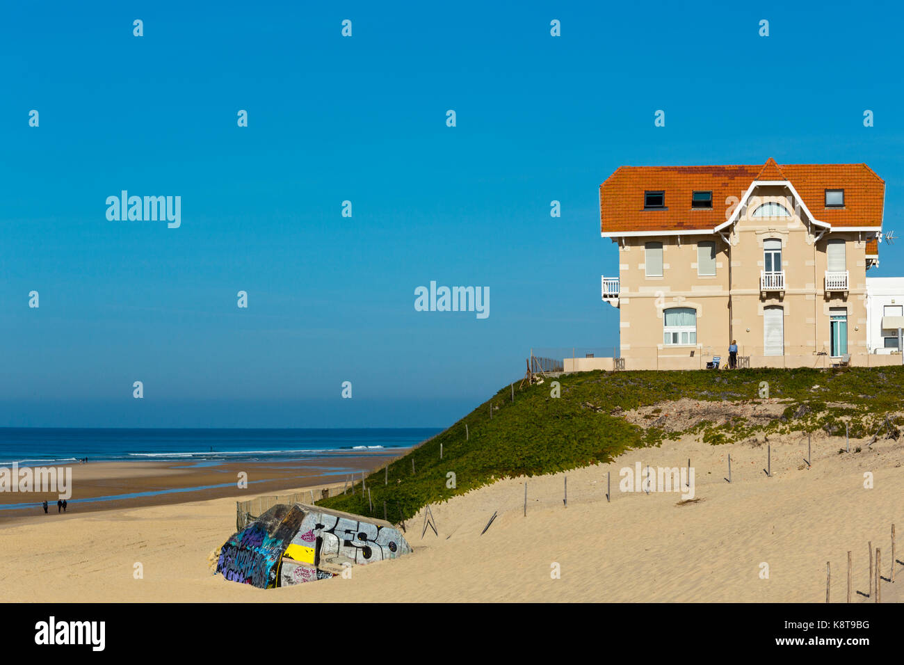 Auf der Seeküste, ein traditionelles Haus vom XIX Jahrhundert. Auf der linken Seite eine der deutschen Bunker aus dem Zweiten Weltkrieg Ruine Th Menschen geht auf den Sand. Stockfoto