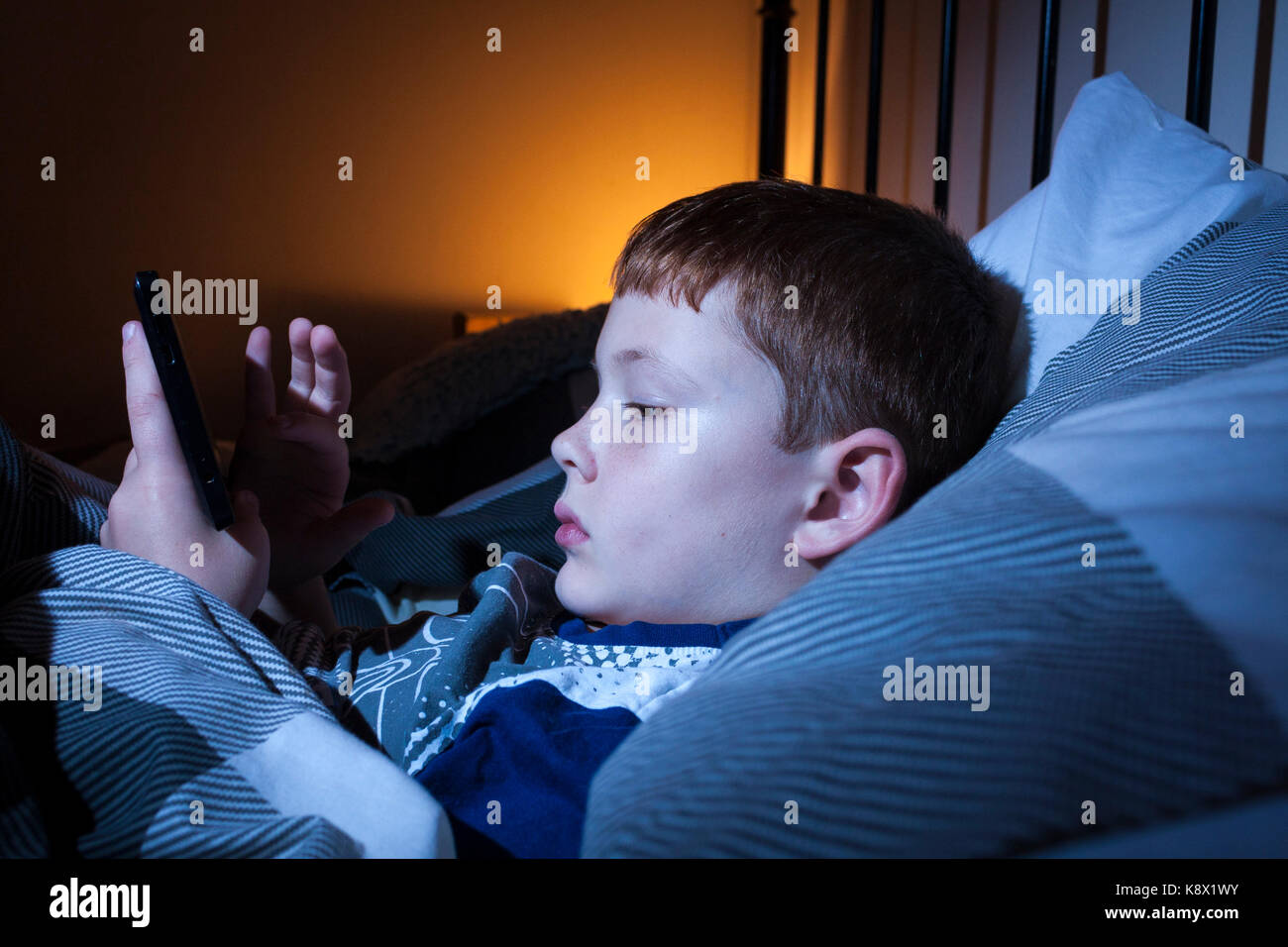 Ein Junge im Bett in der Nacht während der Wiedergabe mit einem Tablet Stockfoto