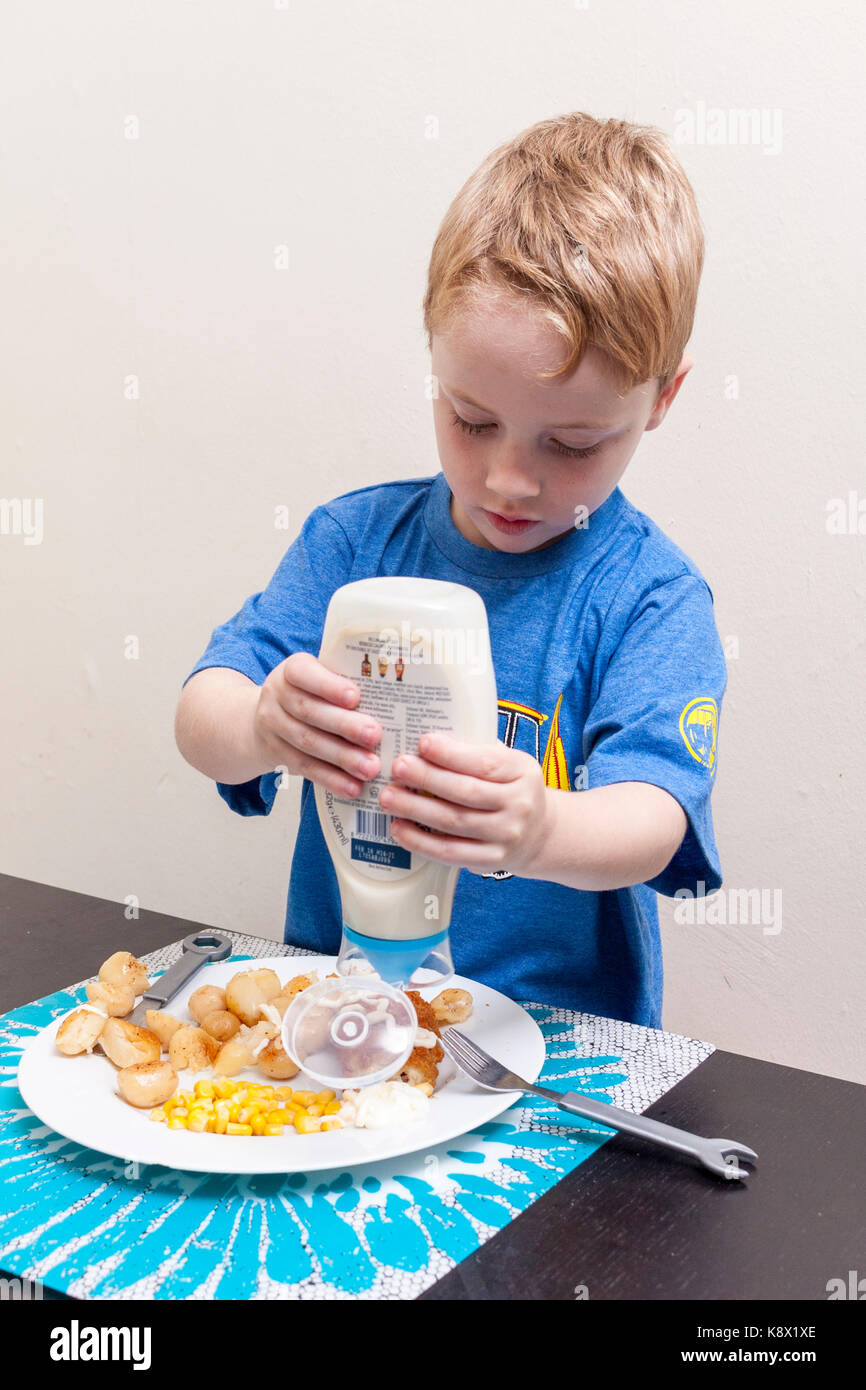 Einem jungen kaukasischen Jungen quetschen Mayonnaise auf seinem Chicken Nugget Abendessen Stockfoto