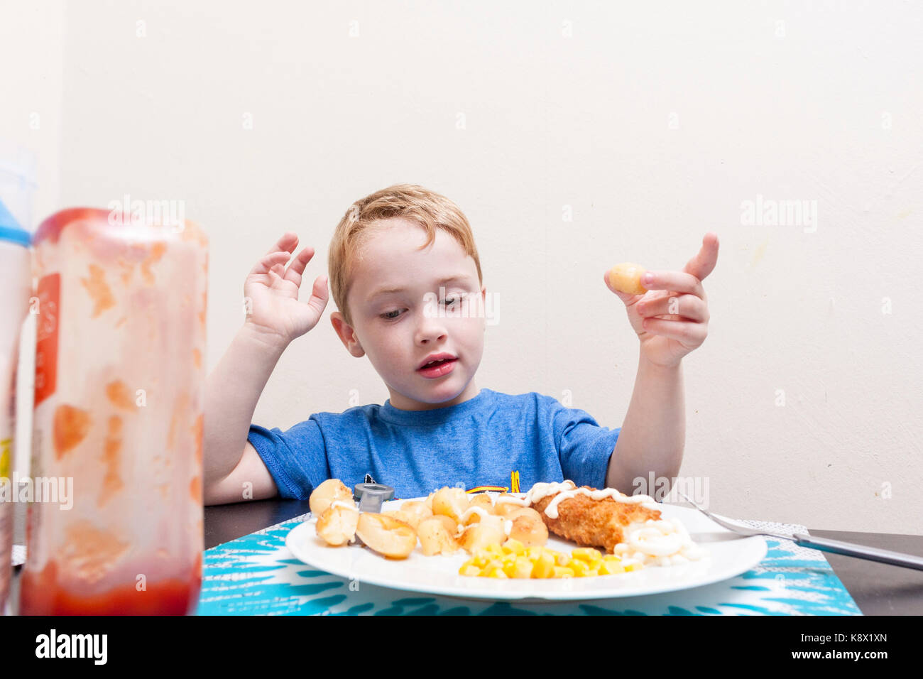 Einem jungen kaukasischen Jungen saßen an einem Tisch sein Abendessen mit Tomaten Ketchup Flasche Essen im Vordergrund. Stockfoto