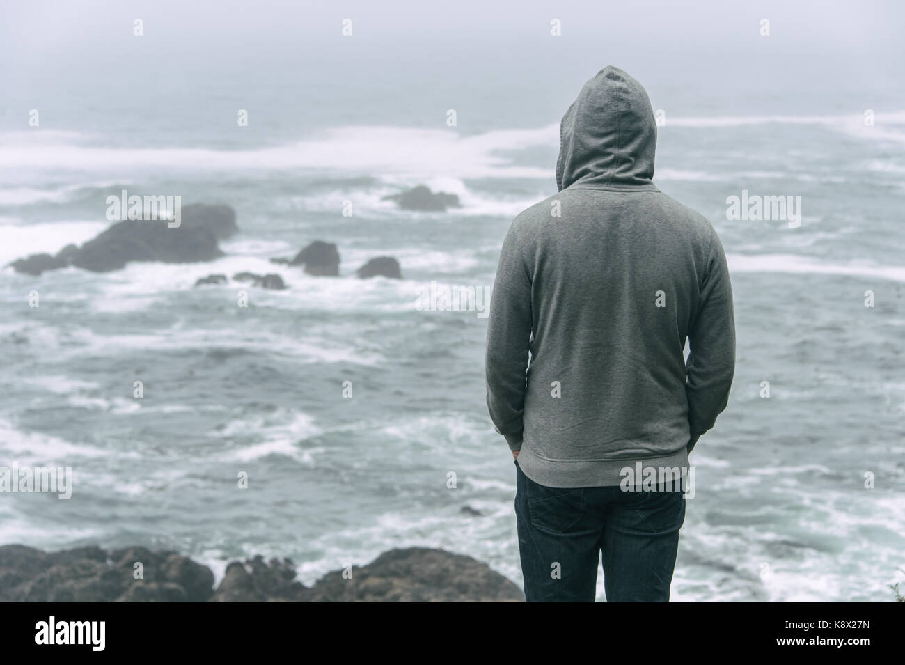 Traurig und einsam Mann, der vor den Pazifischen Ozean und den Blick auf die stürmische See auf Vancouver Island. Stockfoto