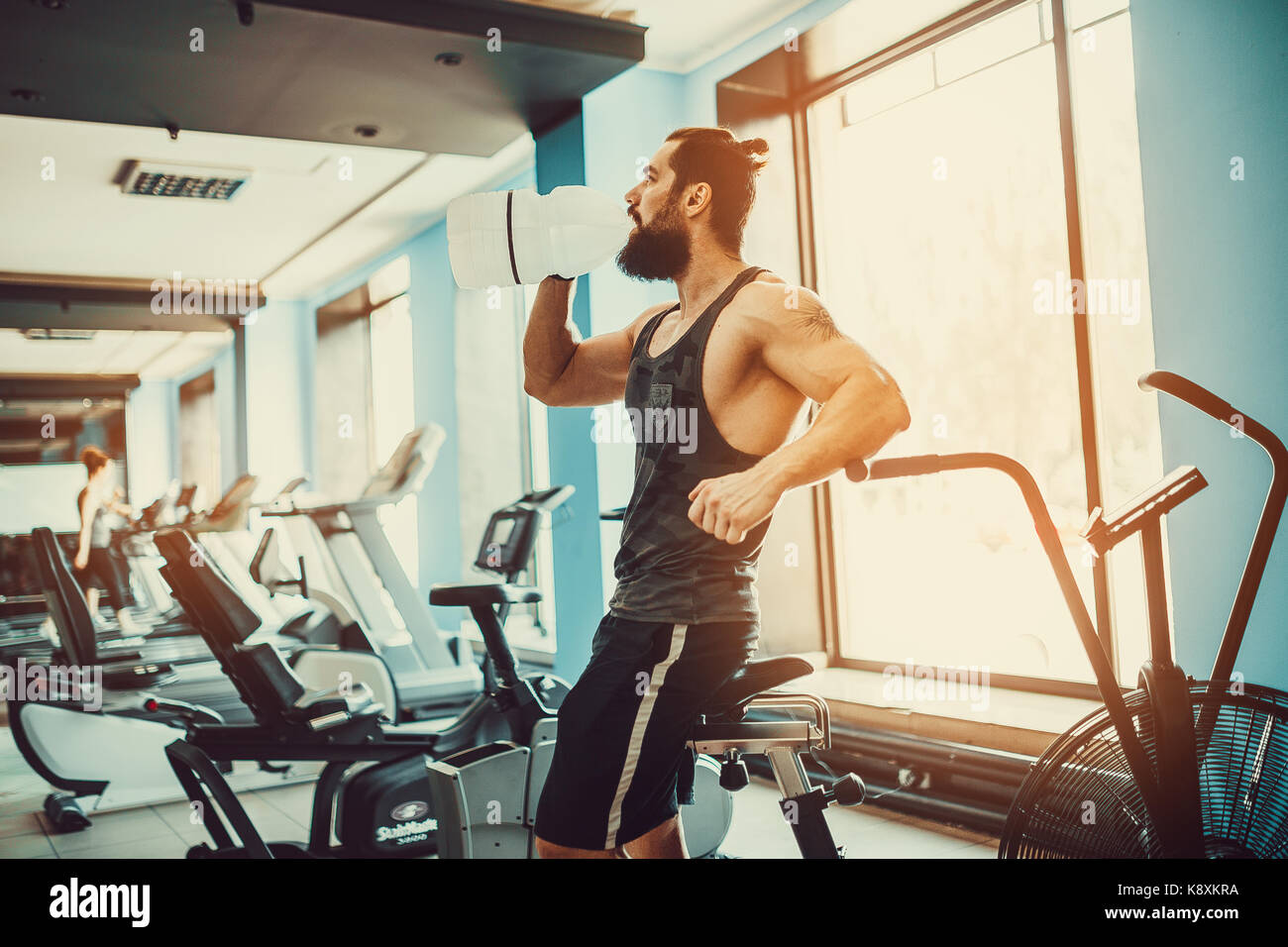 Guy Entspannung nach Training und Halten oder Trinke Wasser aus großen Flasche in der Turnhalle Stockfoto