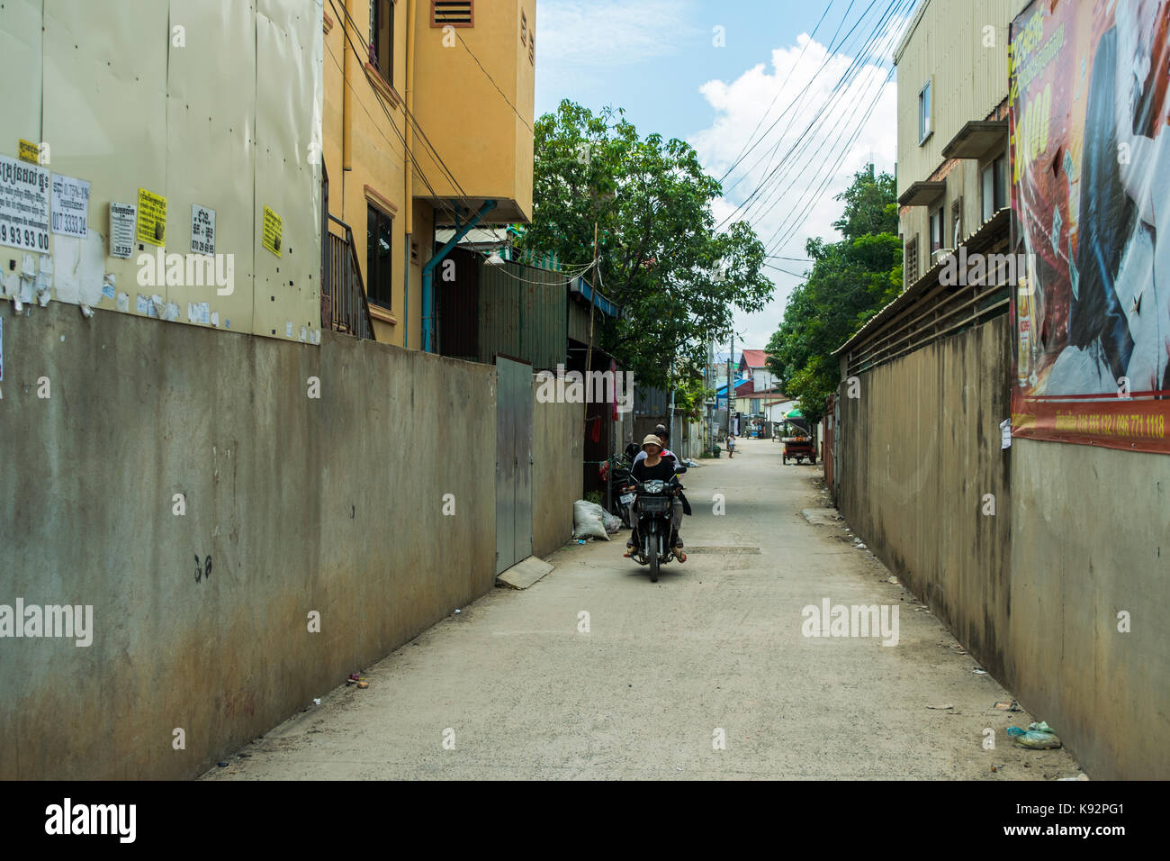 Drei Passagiere, ein Motorrad oder Fahrrad, in einer ruhigen Seitenstraße in Phnom Penh. Eine Frau ist das Fahren, während ein Kind sitzt in der Mitte. Stockfoto