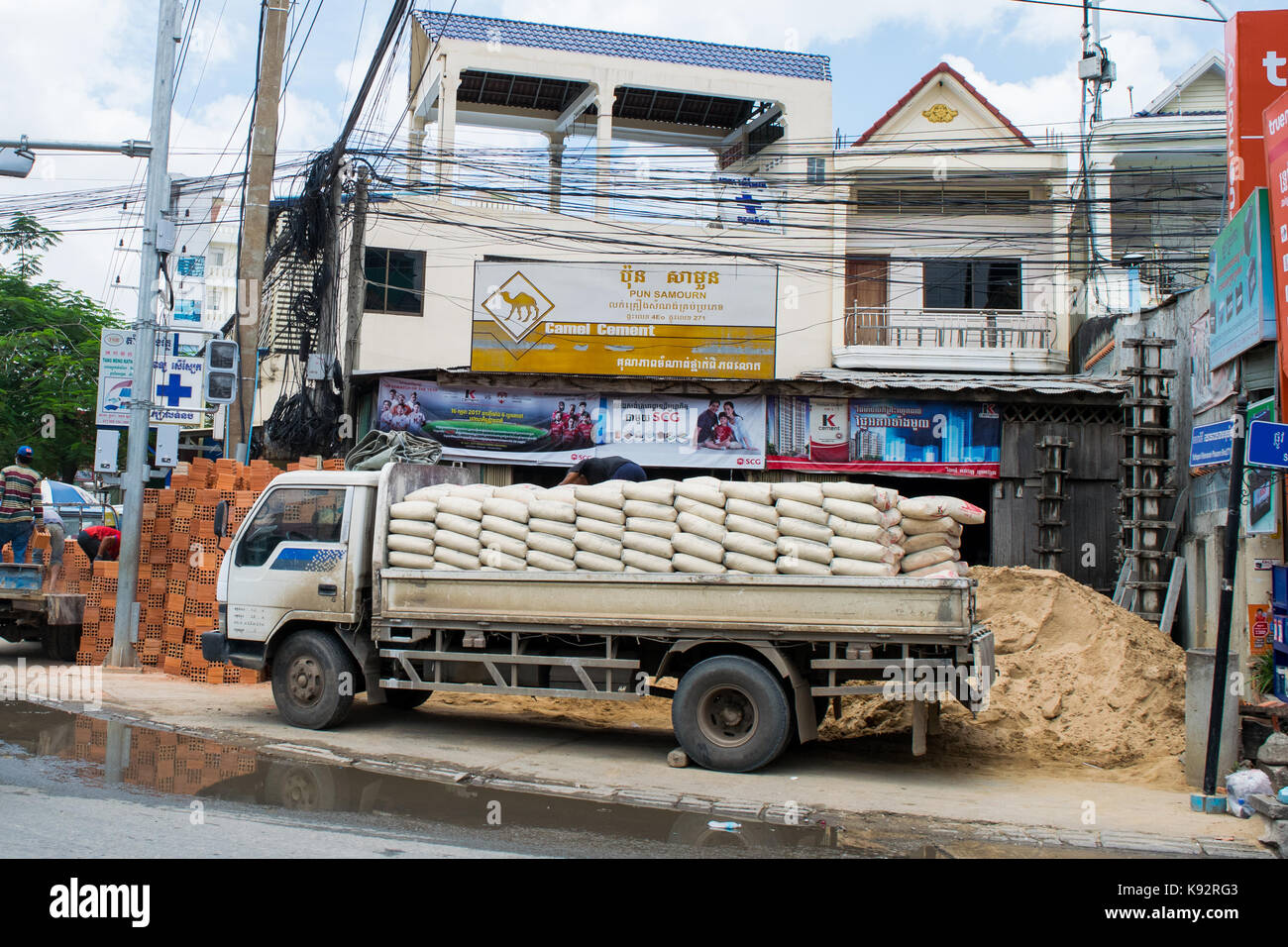 Ein Lkw, beladen mit Sack Zement und auf einem Gehsteig geparkt neben einer Baustelle in Phnom Penh, Kambodscha, Südostasien, Indochina. Stockfoto