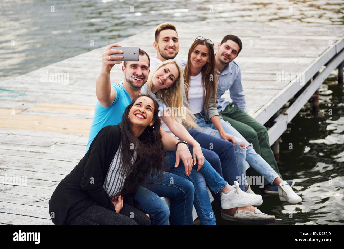 Eine Gruppe junger Leute, die am Rande der Pier und selfie machen. Freunde genießen Sie ein Spiel auf dem See Stockfoto