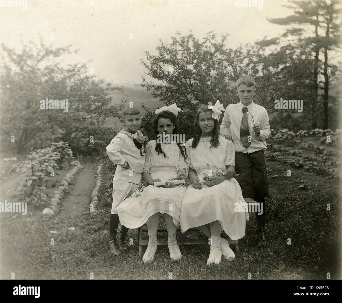 Antike c 1920 Foto, zwei Mädchen in weißen Holding blättert, möglicherweise auf den Tag der Erstkommunion; ein Mädchen trägt ein Kreuz Anhänger. Sie werden durch zwei Jungen flankiert. Lage unbekannt, wahrscheinlich Neu England. Quelle: original Foto. Stockfoto