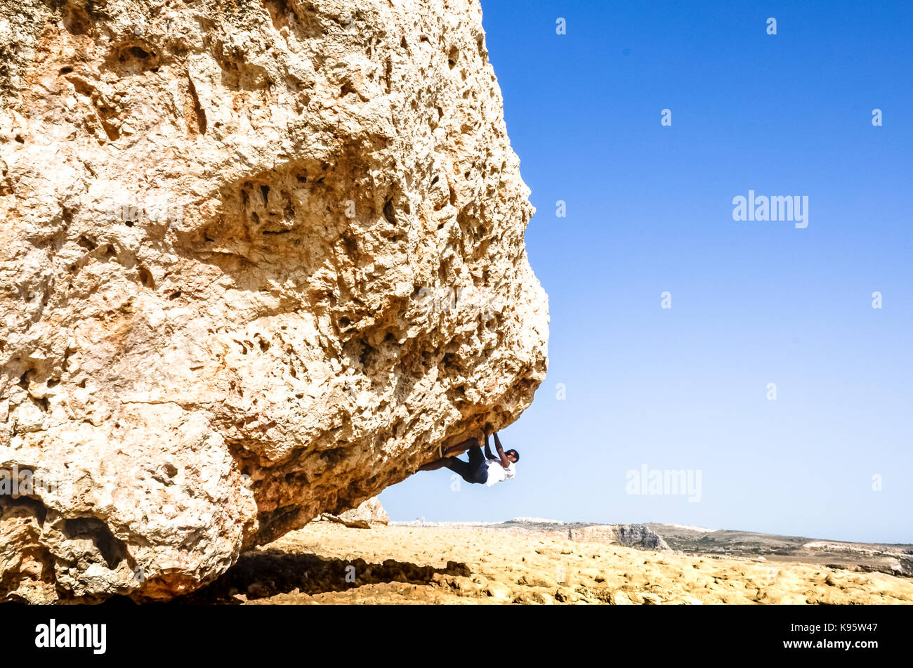 "Gib mir eine Herausforderung, und ich werde es mit Freude erfüllen." Ein Mann klettert ein riesiger Felsen in der robusten Mediterranen Terrain in Malta Stockfoto