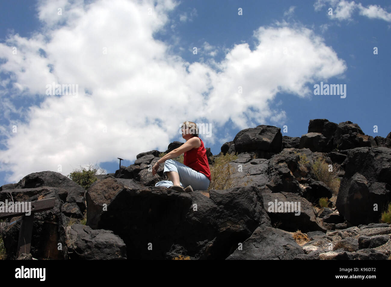 Ältere Frau Wanderungen auf einem steilen Pfad Jagd Felszeichnungen im Petroglyph National Monument in Albuquerque, New Mexico. Sie ruht auf einem großen bould Stockfoto