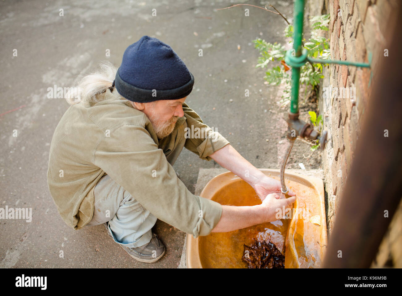 Seitenansicht des Obdachlosen Waschen der Hände in alten Spüle in der Straße. Stockfoto