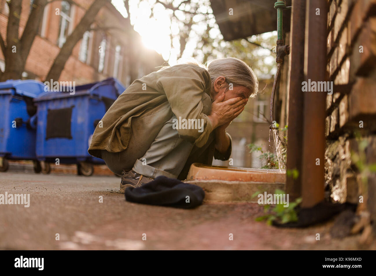 Das Leben auf der Straße, Obdachlosen squating Gesicht zu waschen. Stockfoto