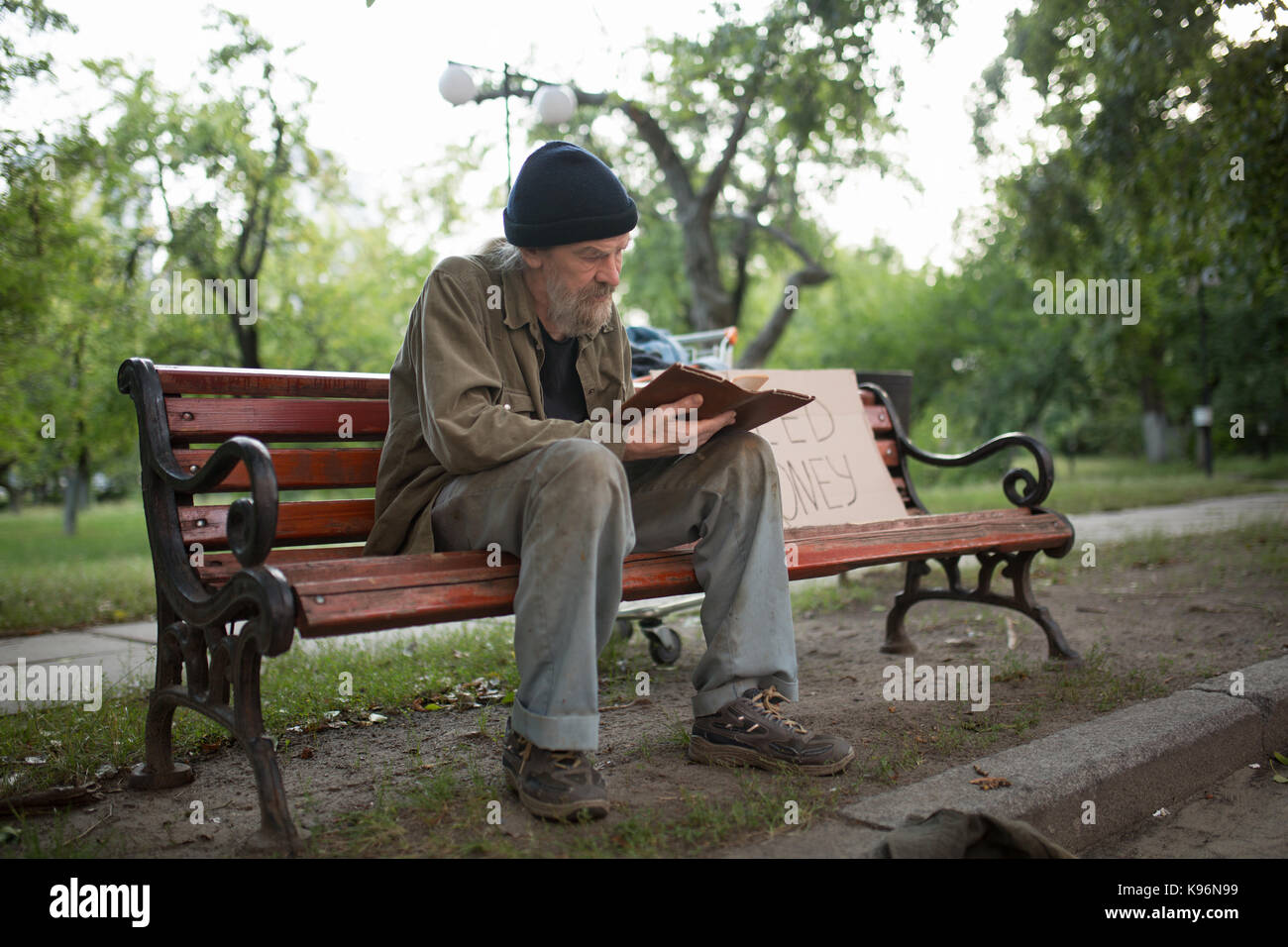 Obdachloser sitzt auf der Bank Holding Buch in den Händen. Stockfoto