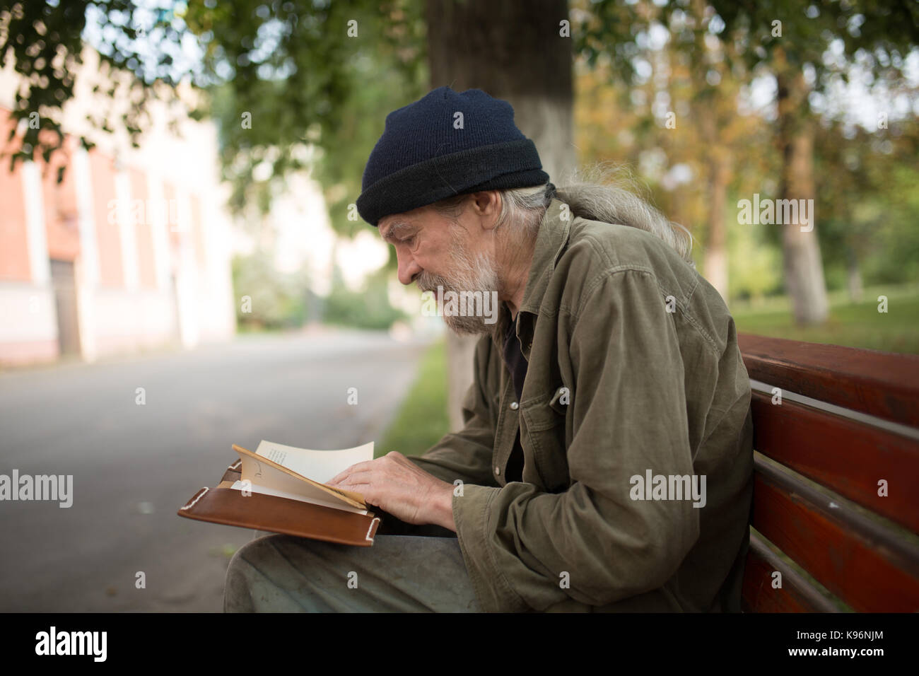 Seitenansicht des Alten obdachlosen Mann mit langen grauen Haaren, ein Buch zu lesen. Stockfoto