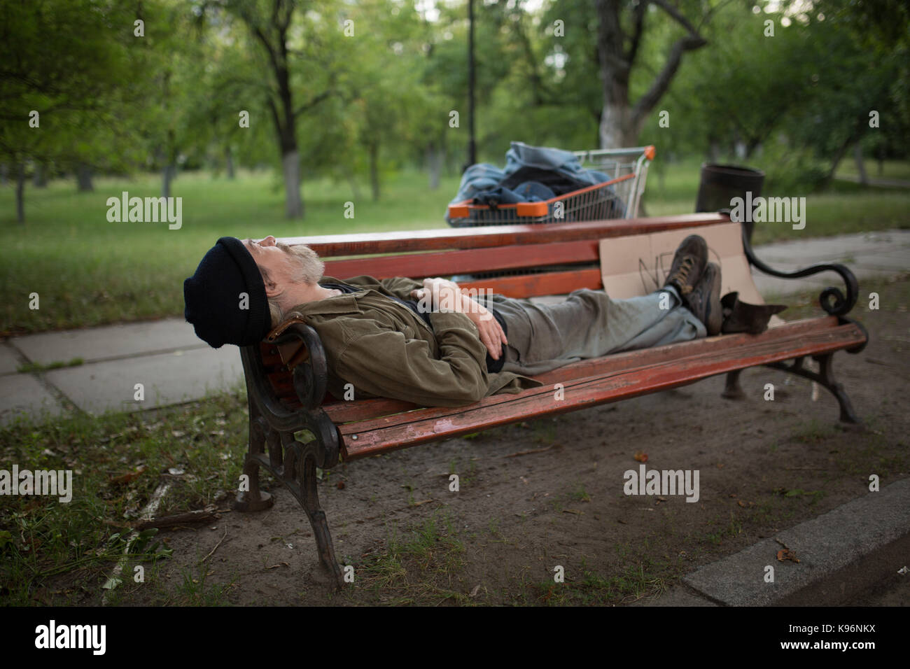 Der alte Mann lag auf der Bank im Stadtpark. Stockfoto