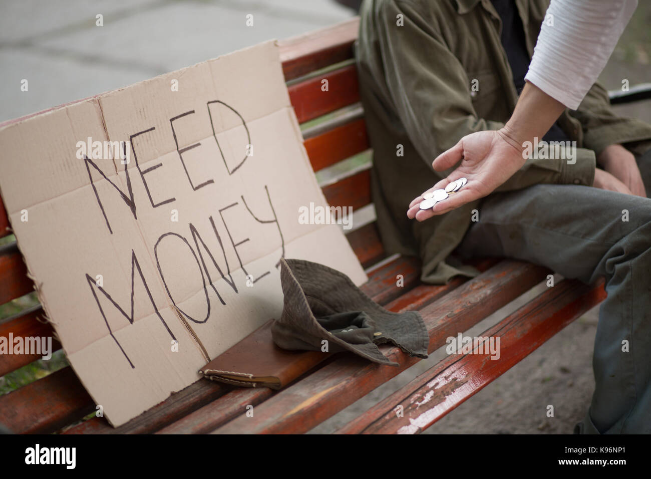 Bild der Bank mit Pappe mit Zeichen brauchen Geld, Hut und Hand mit Münzen. Stockfoto