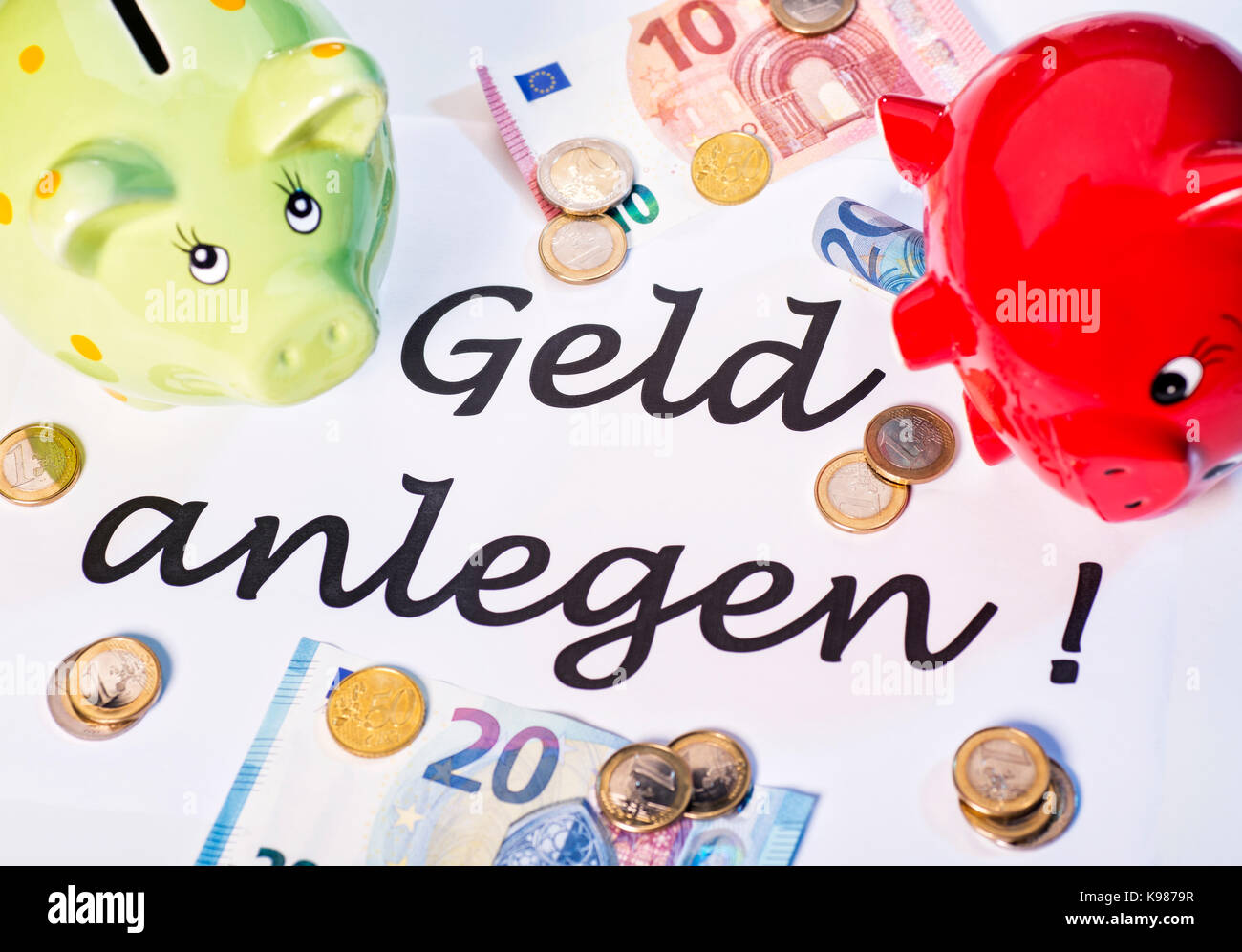 Zwei Sparschweine mit Euro-Münzen und-Banknoten sowie die Worte "Geld zu investieren!". Stockfoto