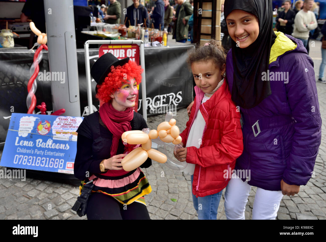 Kinder- Entertainer clown, der Ballon Tiere für die Kinder hier mit einer Familie in Bristol Ereignis Stockfoto