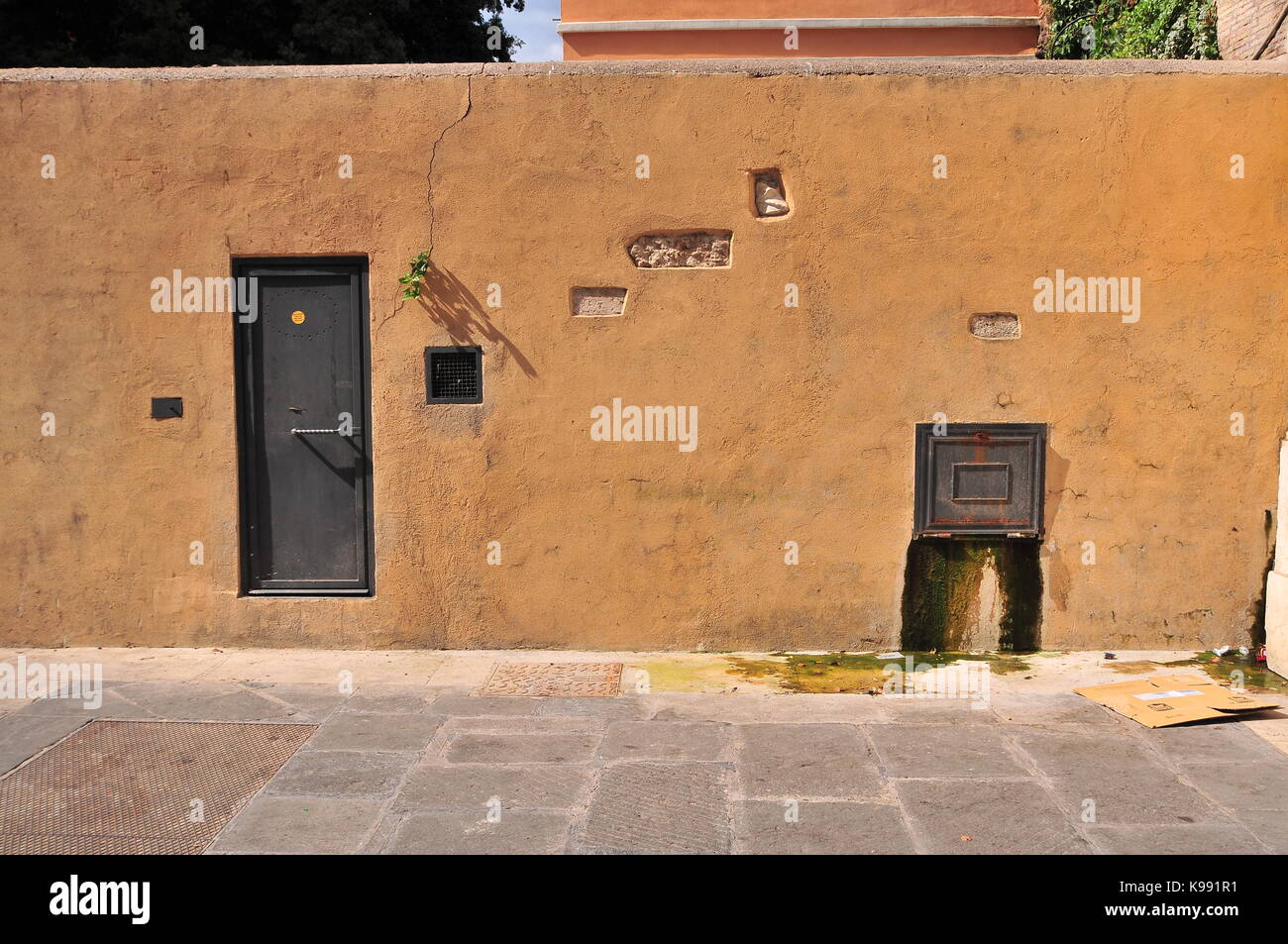 Alte gelbe Wand mit Metalltür und Fleck mit austretendes Wasser. Stockfoto