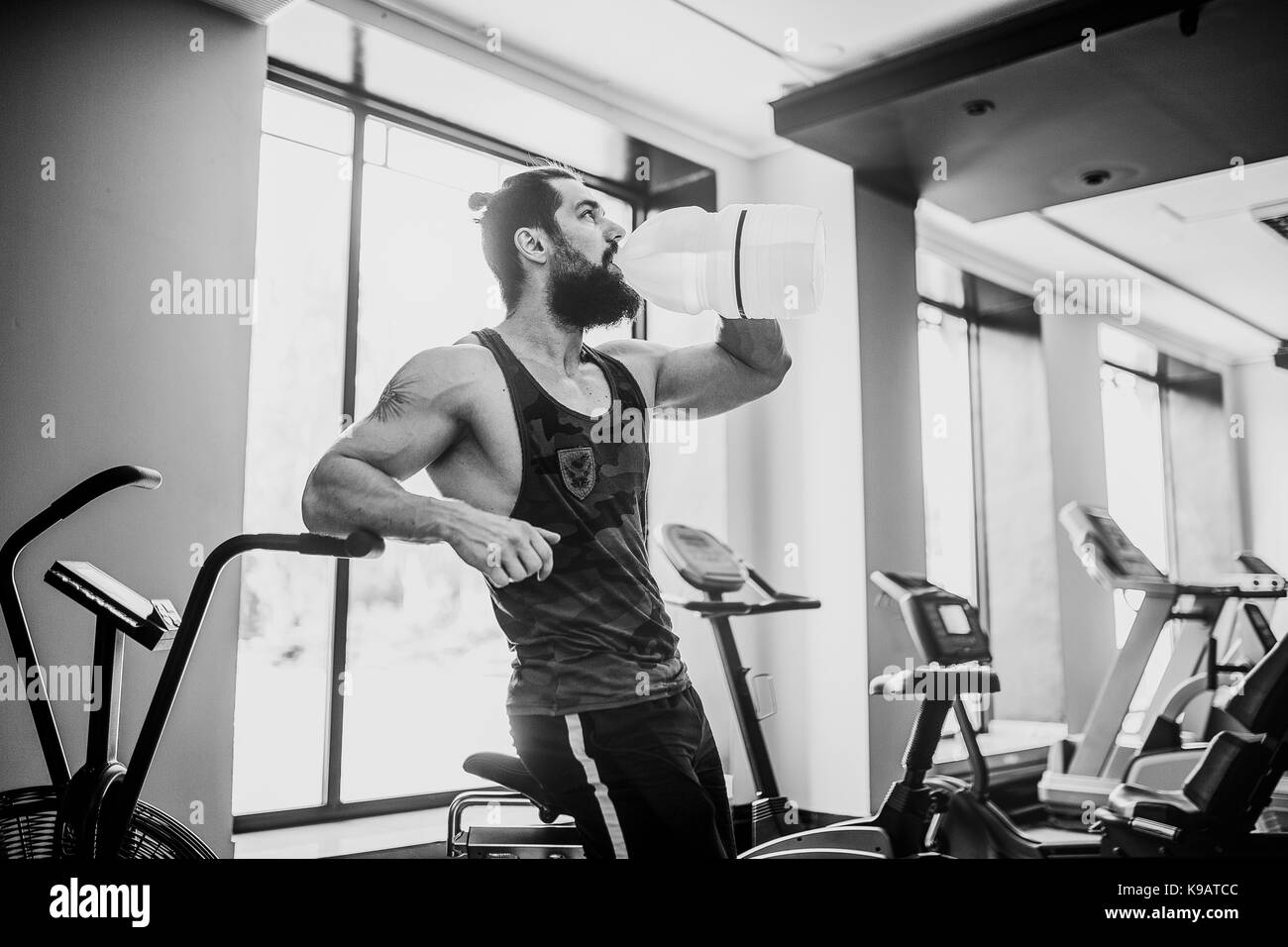 Guy Entspannung nach Training und Halten oder Trinke Wasser aus großen Flasche in der Turnhalle Stockfoto