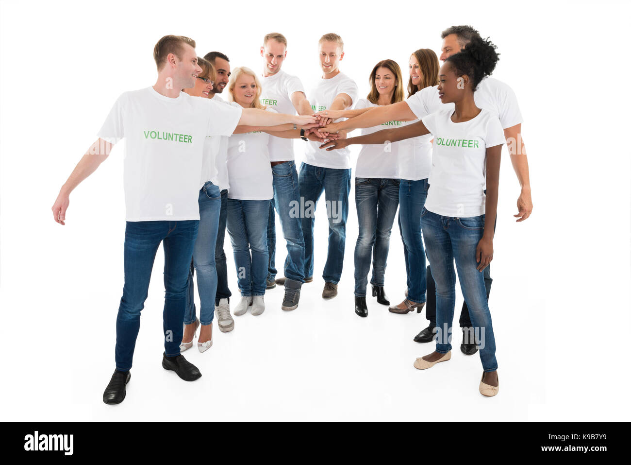 Volle Länge des multiethnischen Freiwillige stapeln Hände beim gegen den weißen Hintergrund stehen Stockfoto