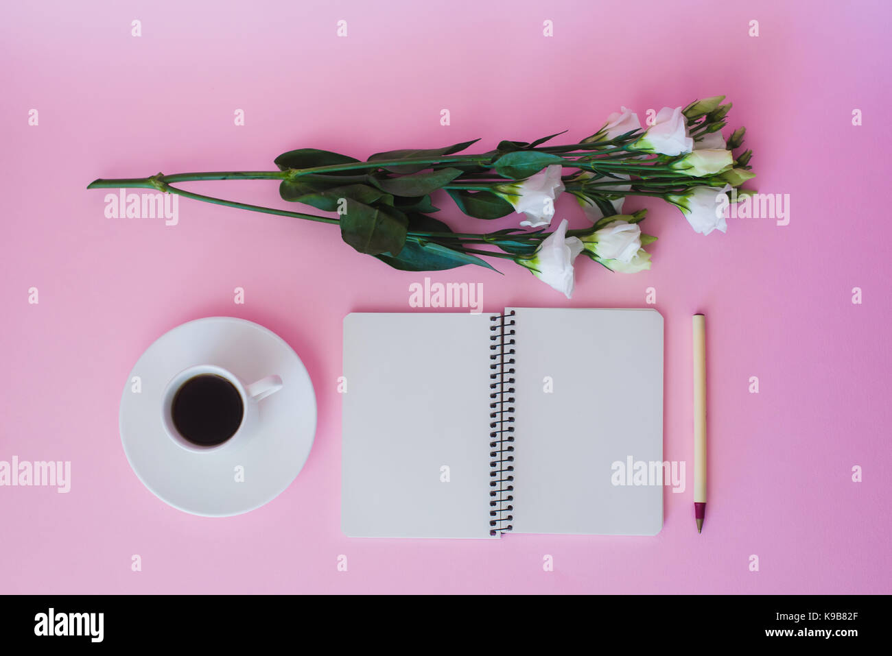 Blick von oben auf die leeren Notizbuch, Stift, Zweig der Blumen und Tasse Kaffee über rosa Hintergrund. Stockfoto